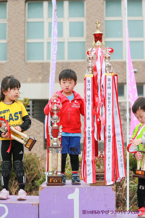 大きなトロフィーの横にたつ男の子